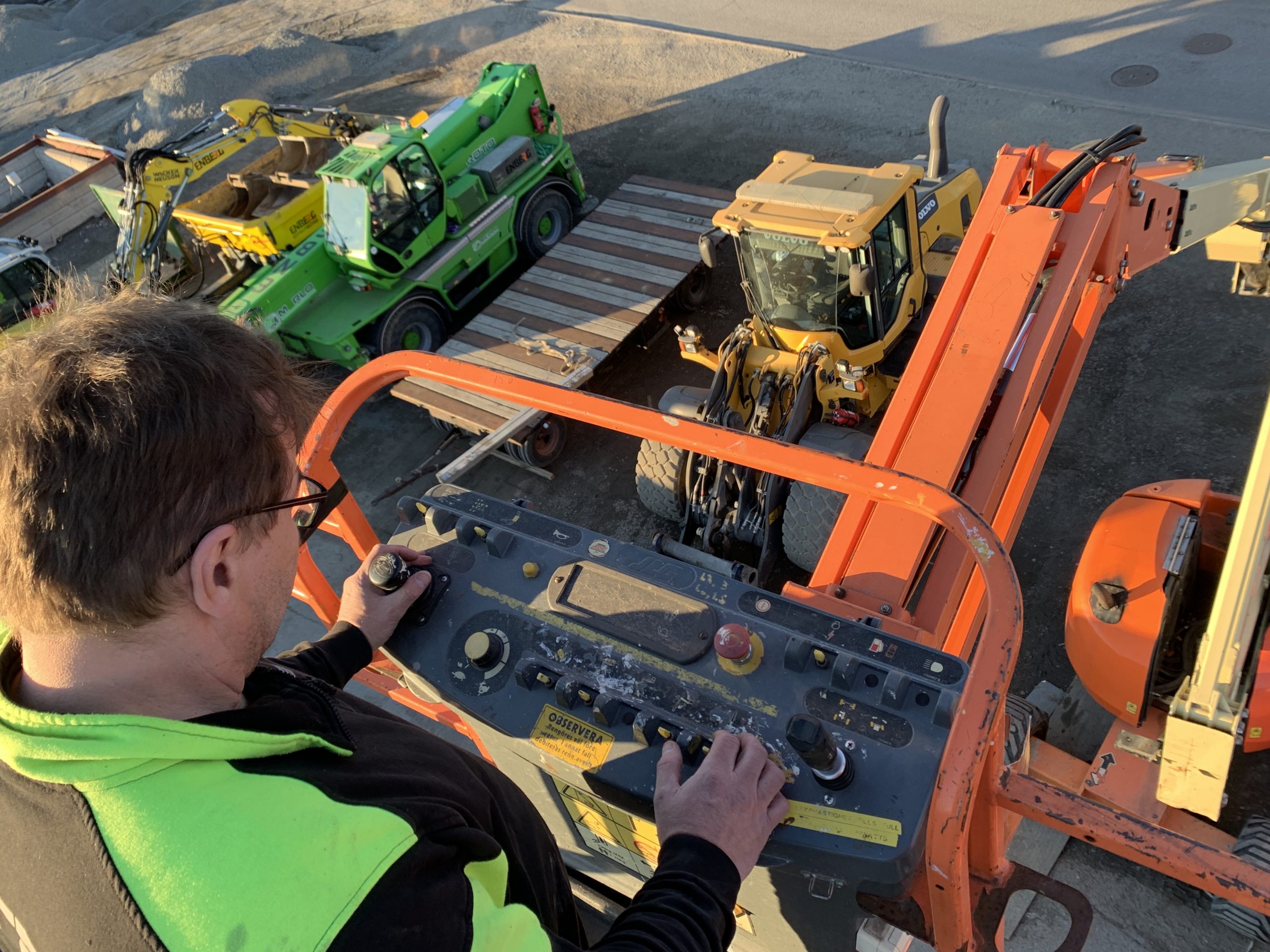 STN-tekniker manövrerar bomlift ovanför uppställningsplats med Merlo- och Volvo-maskiner